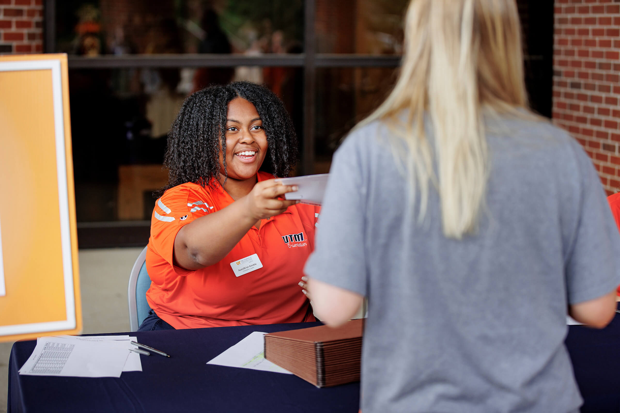 An orientation leader hands a new student a paper schedule at Transfer and Adult Orientation.